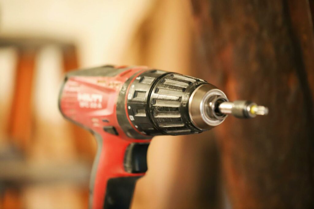 A red electric drill with bit, ready for use on a blurred background.